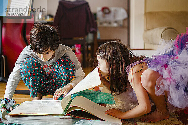 kleines Mädchen im Kostüm nervt Bruder  während er ein Buch liest