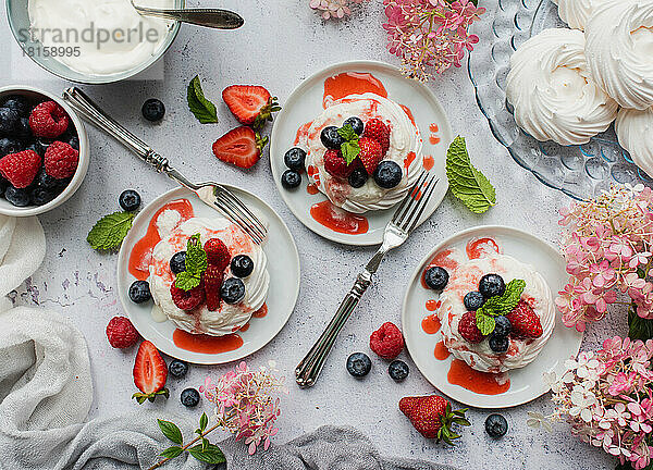 Overhead von Mini-Pavlova-Baiser-Törtchen mit frischen Bieren und Sahne.