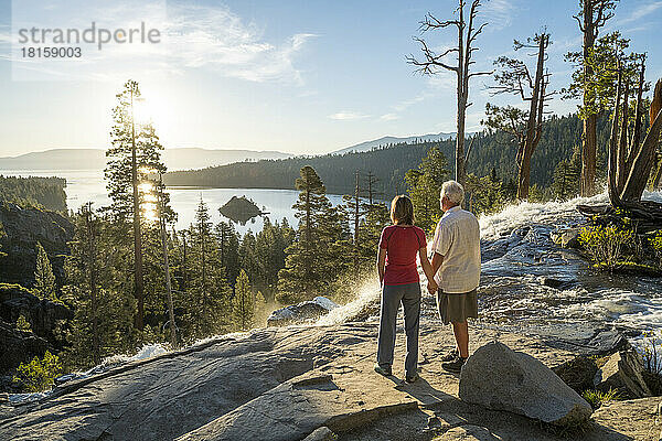 Ein Mann und eine Frau halten sich bei Sonnenaufgang auf dem Gipfel der Eagle Falls an den Händen.