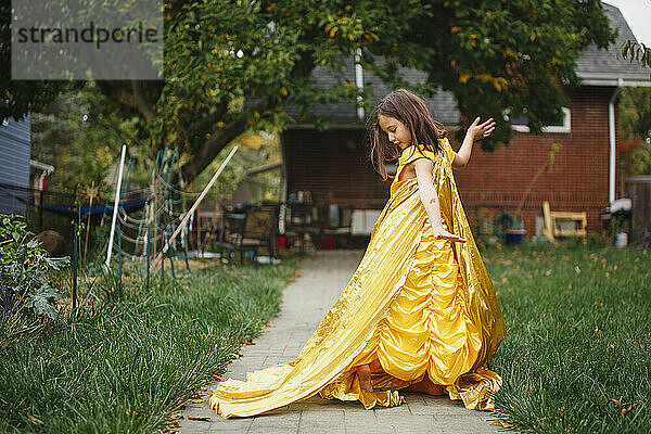 Ein wunderschönes Kind in einem langen goldenen Kleid und einem Umhang tanzt allein draußen