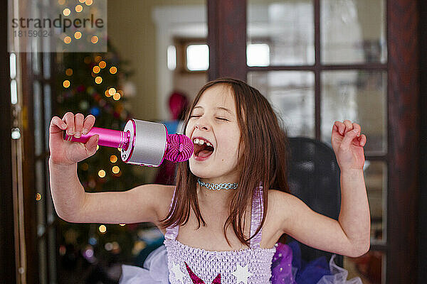 Ein Mädchen im Kostüm singt in einem Mikrofon am Weihnachtsbaum