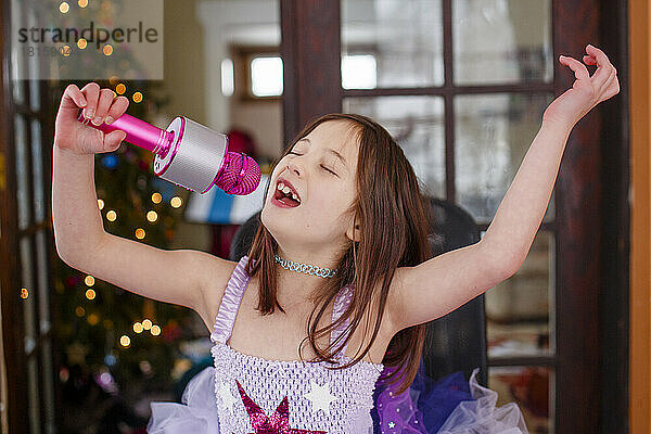 Ein Mädchen mit einem rosa Mikrofon und einem Tutu singt fröhlich allein