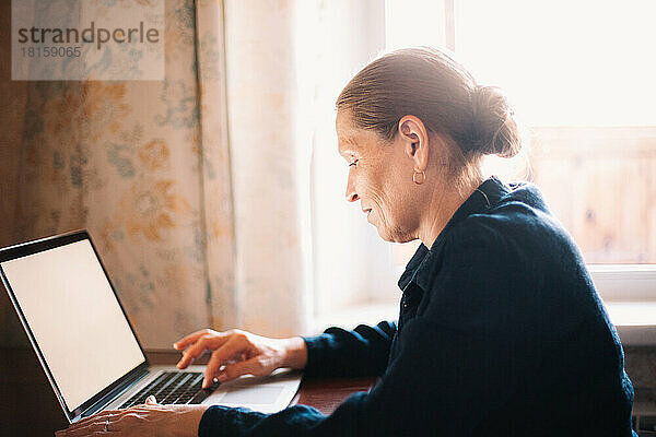 Glückliche reife Frau  die einen Laptop bei der Arbeit zu Hause benutzt