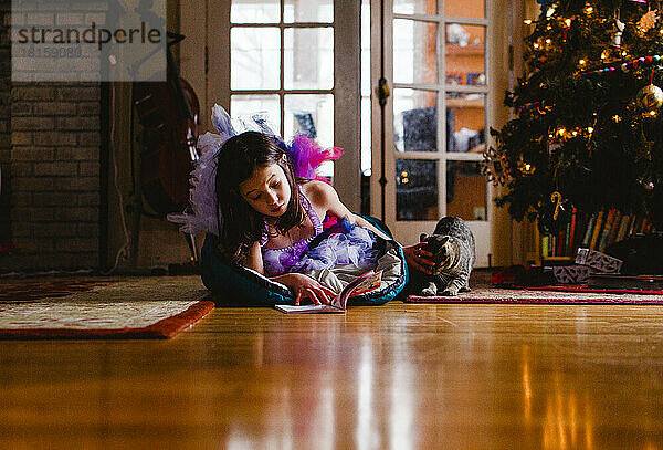 Kleines Mädchen im Kostüm im Schlafsack am Weihnachtsbaum mit Katze