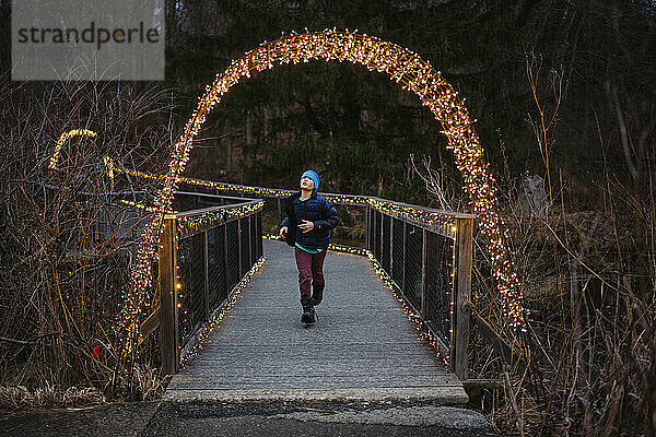 Ein Junge läuft durch eine beleuchtete Brücke in der Abenddämmerung im Winter