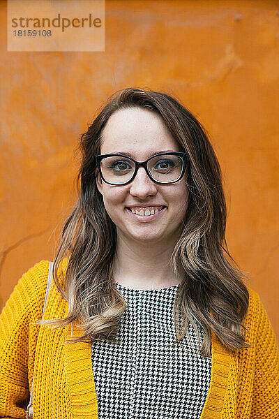 Ein Mädchen mit Brille auf einem orangefarbenen Hintergrund lächelt