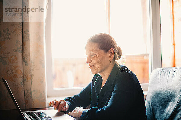 Glückliche lächelnde reife Frau  die einen Laptop bei der Arbeit zu Hause benutzte
