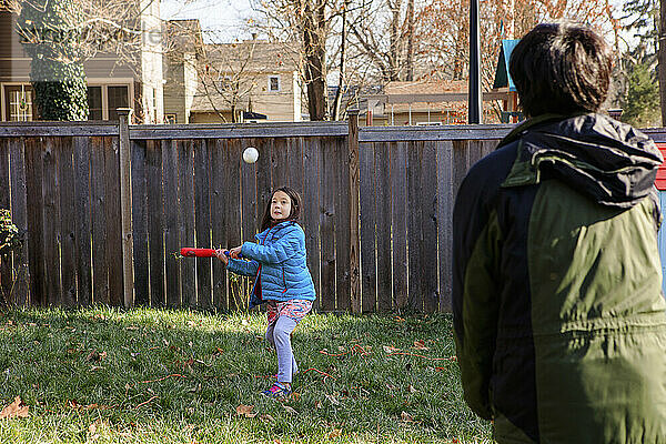 Ein kleines Mädchen spielt Softball mit seinem Vater im Hinterhof im Winter