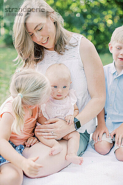 Kleines Mädchen küsst ihre kleine Schwester auf die Wange  während sie mit ihrer Familie zusammensitzt.