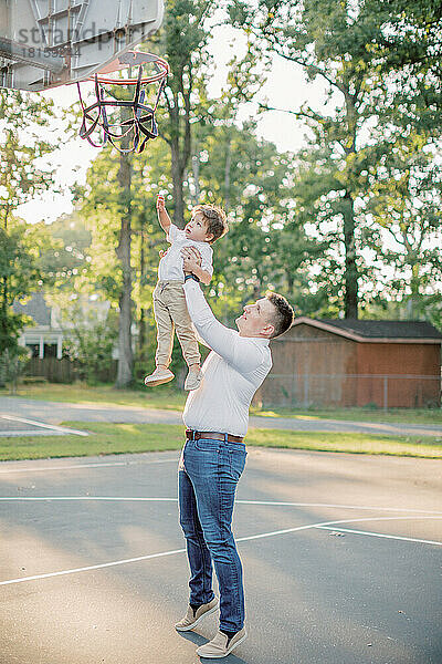 Ein 30-35 Jahre alter Vater hebt seinen 2-jährigen Sohn zum Basketballnetz.