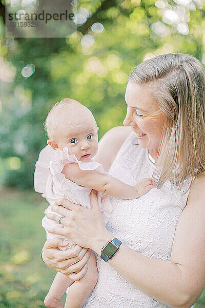 Ein 4 Monate altes Mädchen blickt in die Kamera  während die Mutter es hält und anlächelt.