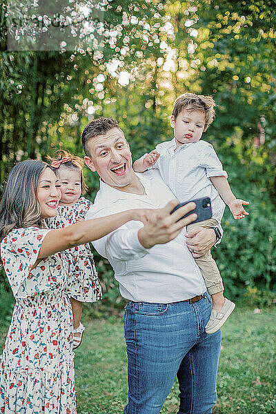 Eine gemischtrassige Familie mit zwei Kindern macht ein Selfie mit ihrem Mobiltelefon.