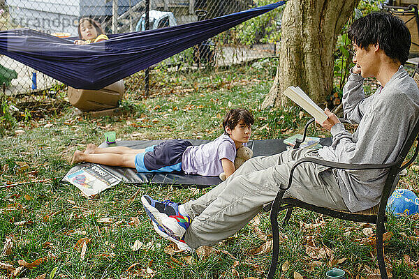 Ein Vater liest seinen Kindern draußen im Hinterhof ein Buch vor