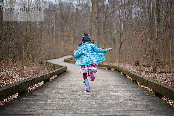 Ein Kind in hellen bunten Kleidern läuft den Pfad im Wald hinunter