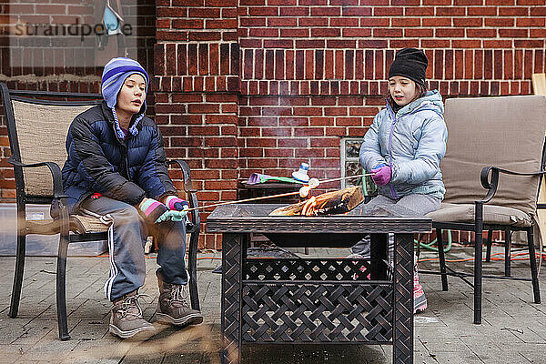 Zwei Kinder rösten im Winter Marshmallows über einer Feuerstelle im Hinterhof