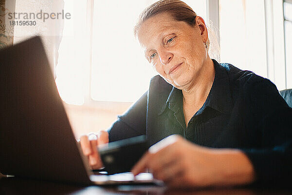 Ältere Frau mit Laptop und Kreditkarte beim Online-Shopping