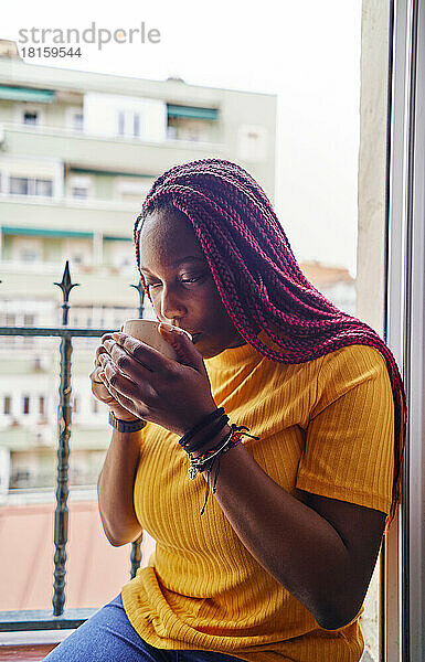 Afroamerikanische Frau trinkt Kaffee am Küchenfenster sitzend