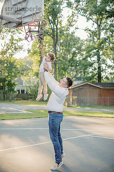 Kaukasischer Vater hält seinen 2-jährigen Sohn an den Basketballkorb.