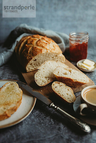 Draufsicht auf einen geschnittenen Laib Brot mit Butter  Marmelade und Kaffee.