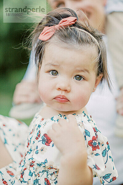 1 Jahr altes Mädchen mit haselnussbraunen Augen in geblümtem Kleid.