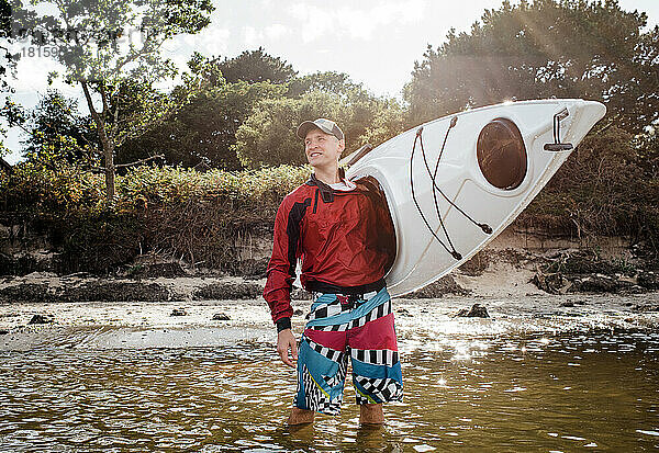 Ein Mann stand fröhlich im Meer und hielt ein Kajak in der Hand  bereit für ein Abenteuer.