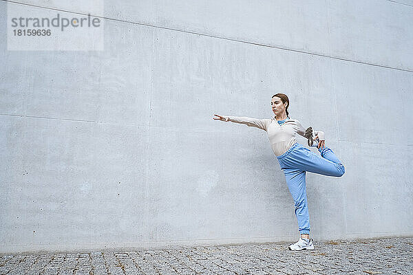 Mädchen in blauer Hose streckt sich und tanzt gegen eine graue Wand