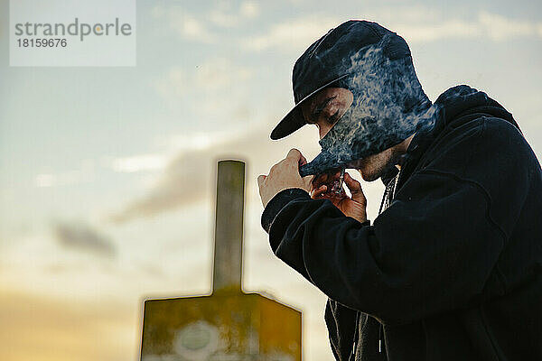 Mann mit Sturmhaube raucht einen Joint Marihuana im Freien