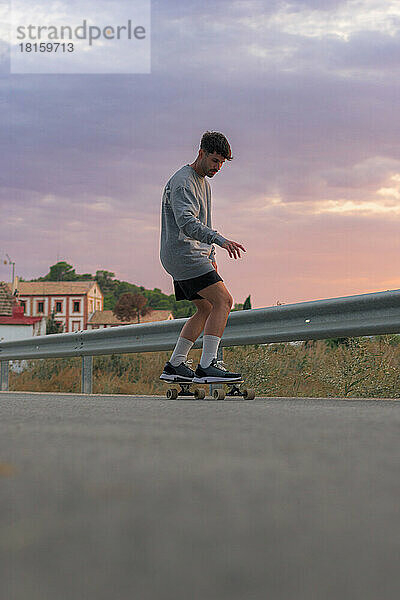 Junger Mann auf einem Skateboard auf der Straße bei Sonnenuntergang