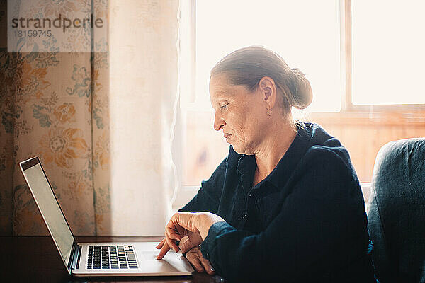 Ernsthafte reife Frau  die einen Laptop benutzt  während sie zu Hause arbeitet