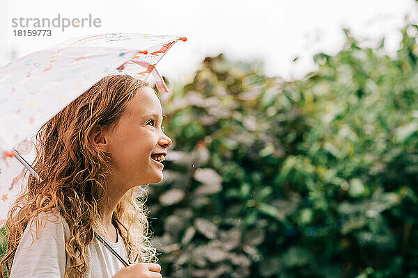 lachendes Kind  das draußen im Regen einen Regenschirm hält