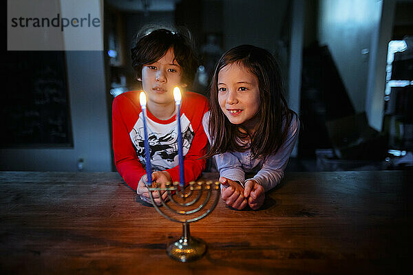 Zwei Kinder sitzen zusammen am Tisch und betrachten die beleuchtete Menora zu Hannukah