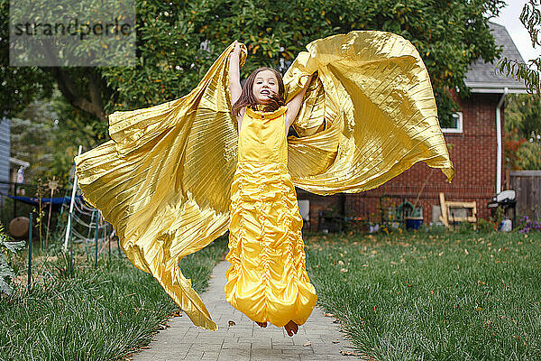 Ein engelhaftes kleines Mädchen in goldenem Kleid und langem Umhang springt in die Luft