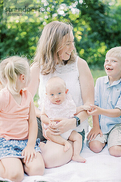 Mutter sitzt und lächelt ihre 3 kleinen Kinder in einem Park an