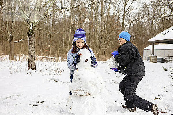 Zwei glückliche Kinder bauen im Winter gemeinsam einen Schneemann