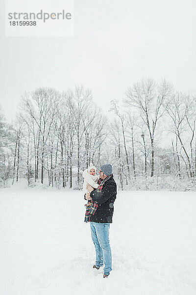 Ein 30-jähriger Vater hält sein 12 Monate altes Baby auf einem verschneiten Feld.