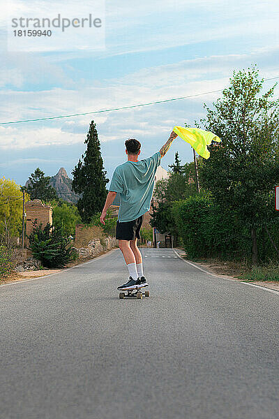 Junger Mann auf einem Skateboard auf einer Straße mit einem reflektierenden Kleidungsstück