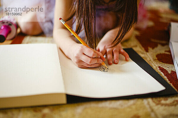 Nahaufnahme eines Kindes  das sorgfältig mit einem Bleistift in einem Skizzenbuch zeichnet