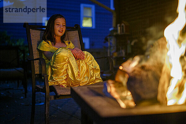 Ein fröhliches Kind im Kostüm sitzt nachts am Lagerfeuer