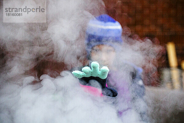 Ein Kind streckt seine Hand mit dem Handschuh durch eine Rauchwolke