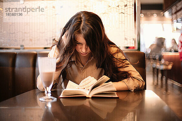 Teenager-Mädchen  das in einem Café sitzt und ein Buch liest