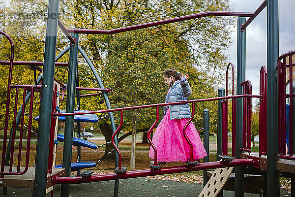 Ein kleines Mädchen in einem rosa Kostüm spielt auf einem Spielplatz im Herbst