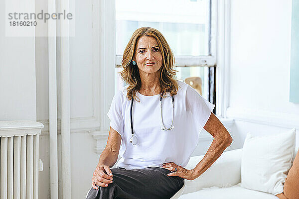 Porträt einer selbstbewussten Ärztin  die auf einem Tisch im Krankenhaus sitzt