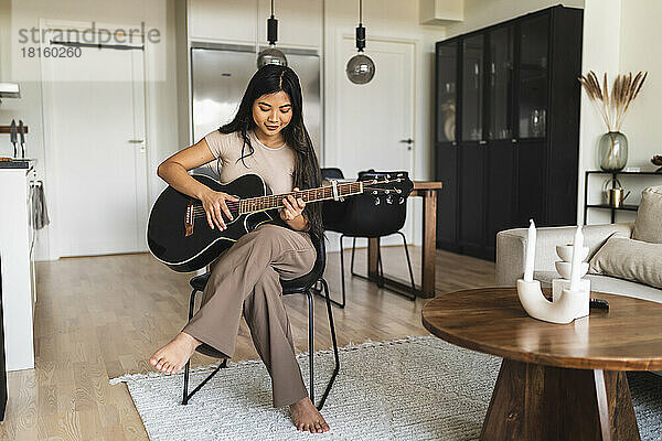Young woman playing guitar sitting at home