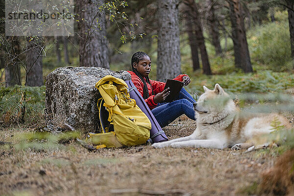 Junge Frau liest Buch und sitzt mit Hund im Wald