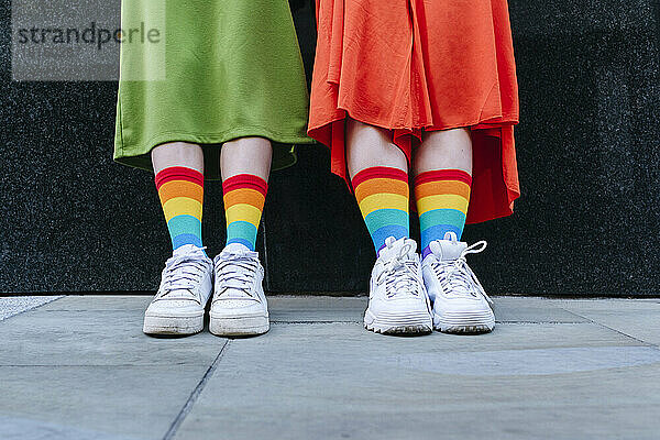 Gemischtrassiges lesbisches Paar trägt bunte Socken vor der Wand