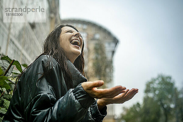 Cheerful woman in raincoat enjoying rain