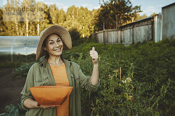 Lächelnde reife Frau mit einer Schüssel grüner Erbsen gestikuliert im Garten