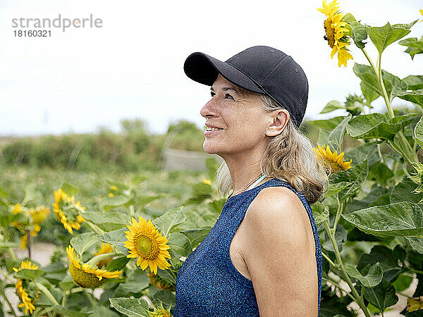 Lächelnde ältere Frau vor Sonnenblumenpflanzen