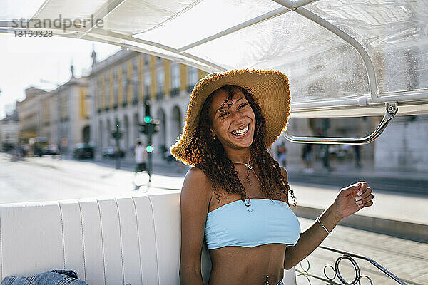 Fröhliche junge Frau mit Hut macht an einem sonnigen Tag eine Tuk-Tuk-Fahrt