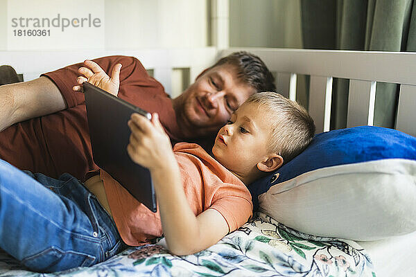 Sohn und Vater schauen zu Hause auf den Tablet-PC  der im Bett liegt